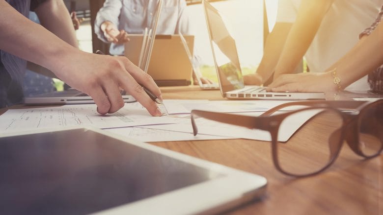 A group of people sitting around a table with laptops and papers.