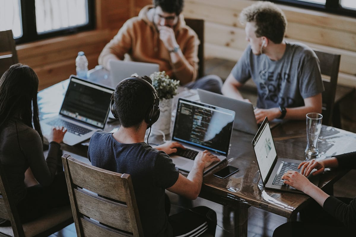 Five people are seated around a table working on laptops in a modern, wood-paneled room.