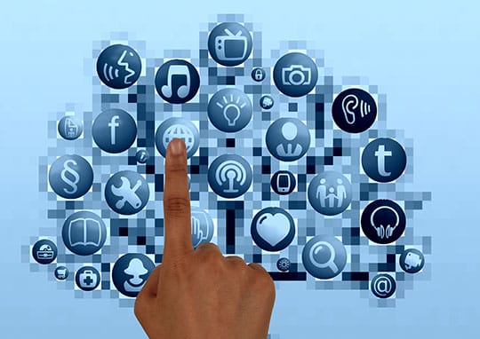 A hand points to a globe icon on a screen displaying a network of various digital icons, including social media, communication, and multimedia symbols.