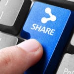 A finger presses a blue keyboard key labeled SHARE with a share icon, surrounded by standard black and gray keys.
