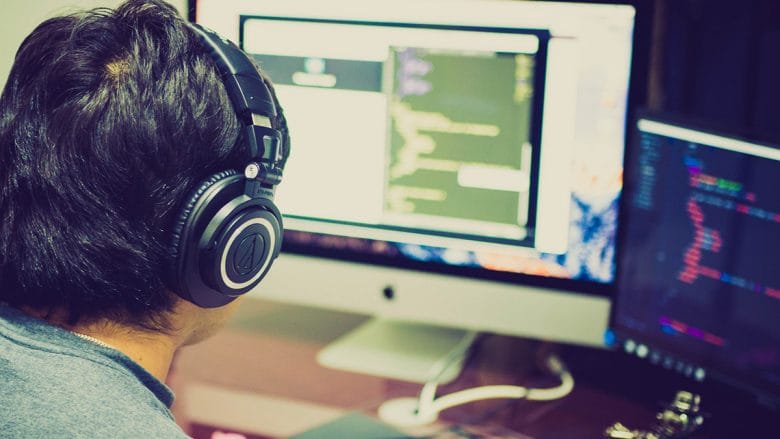A person with headphones is working on a computer with multiple screens displaying code.