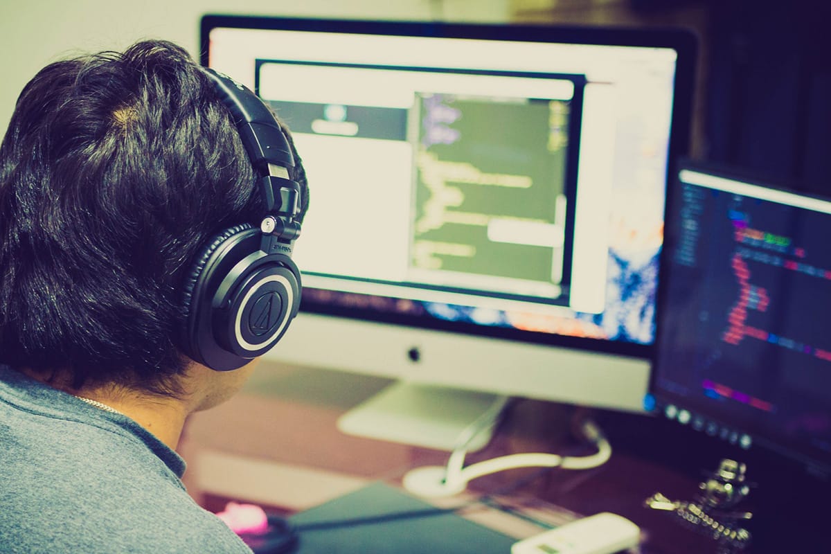 A person with headphones is working on a computer with multiple screens displaying code.