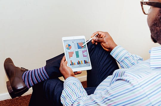 Person using a stylus on a tablet displaying colorful graphs, wearing striped socks and sitting with legs crossed.