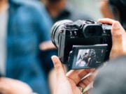 Person holding a camera, capturing an image of two people displayed on the camera's screen.