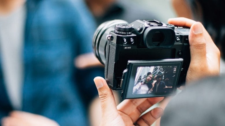 Person holding a camera, capturing an image of two people displayed on the camera's screen.