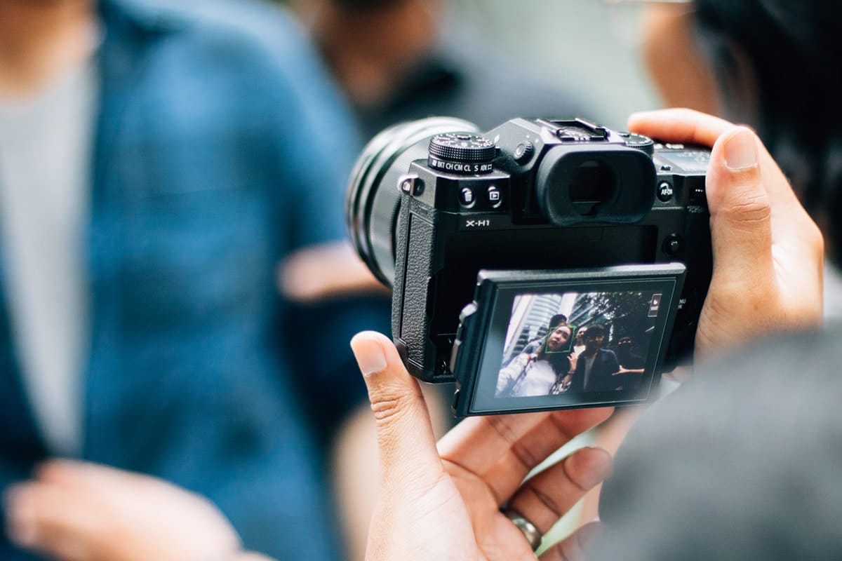 Person holding a camera, capturing an image of two people displayed on the camera's screen.