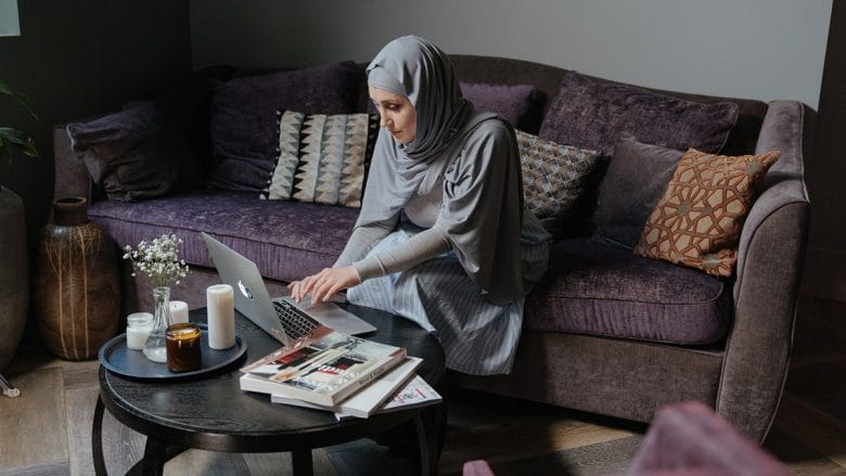 A muslim woman using a laptop in her living room.