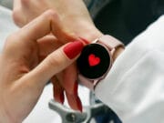 Close-up of a person with red nails touching a smartwatch displaying a red heart on the screen.