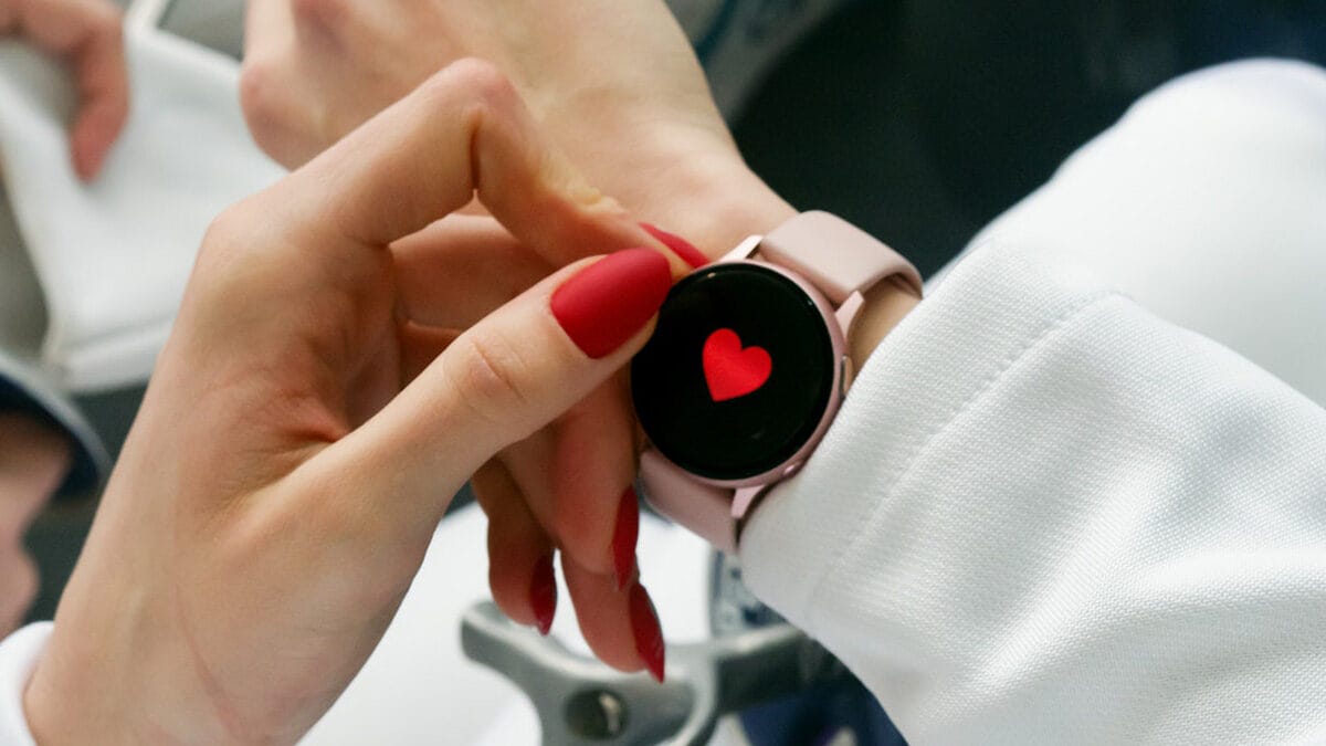 Close-up of a person with red nails touching a smartwatch displaying a red heart on the screen.