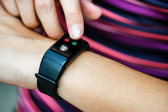 A person wearing a black wristband smartwatch is touching the screen to answer an incoming call shown on the display.