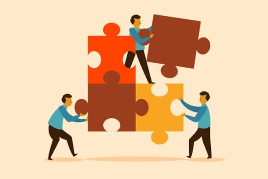 Three people in blue shirts assemble large puzzle pieces in red, brown, and yellow tones, symbolizing teamwork and collaboration.