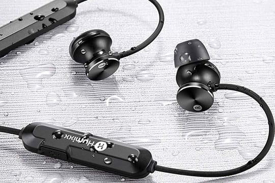 Black waterproof earbuds with a neckband and control panel shown on a wet surface, with water droplets on the earbuds and cable.