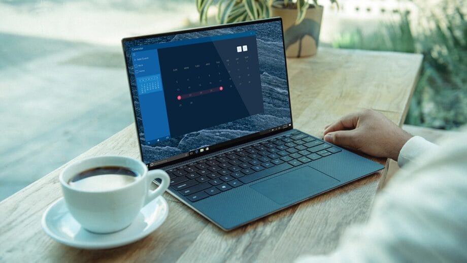 A person working on a laptop next to a cup of coffee on a wooden table.