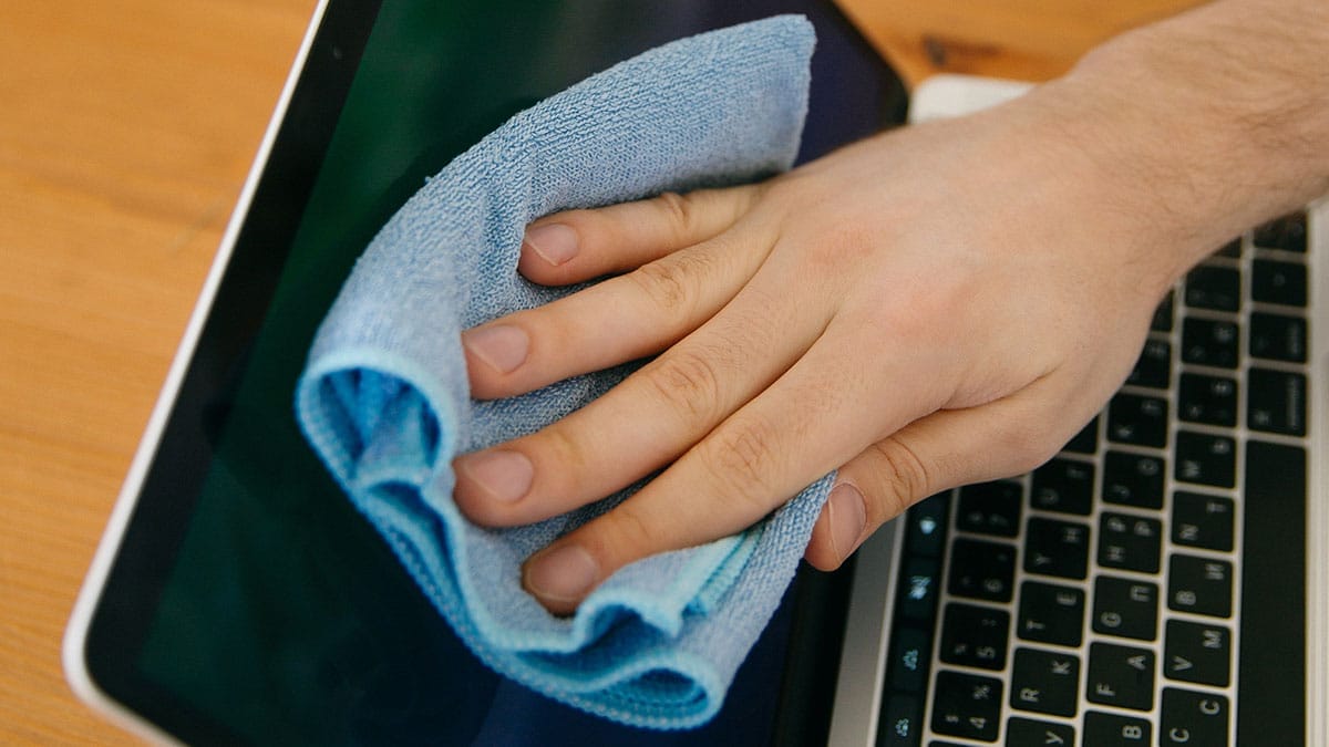 A person is cleaning a laptop screen with a blue microfiber cloth.