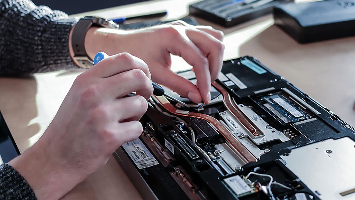 A person is disassembling or repairing a laptop, using a screwdriver to work on the internal components.