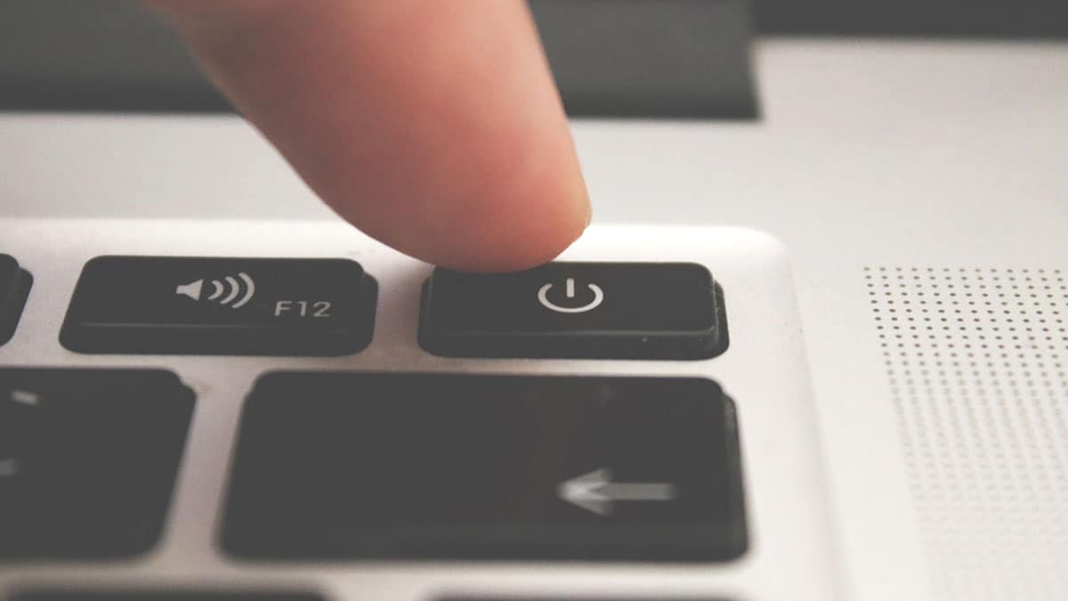 A finger pressing the power button on a laptop computer keyboard.