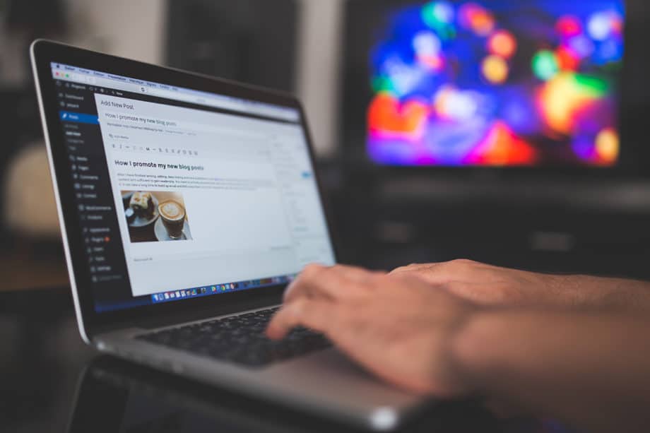 A person writing a blog post in wordpress dashboard on a laptop computer in front of a tv.