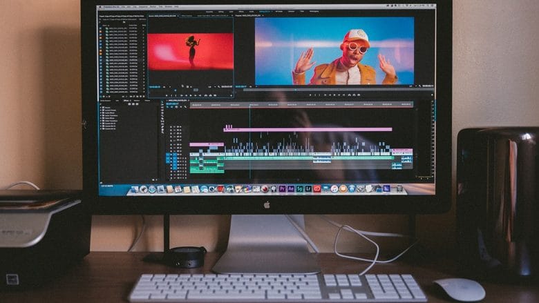 A desktop computer displaying video editing software with a music video in progress, featuring a person wearing red sunglasses and a white cap.