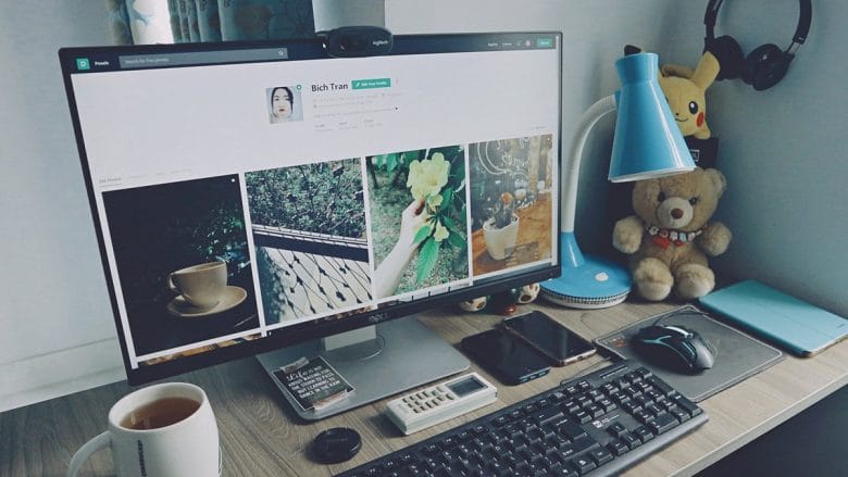 A well-organized desk with a computer displaying a social media profile, surrounded by various office items including a cup of coffee, headphones, a notepad, a smartphone, a calculator, and some decorative objects.