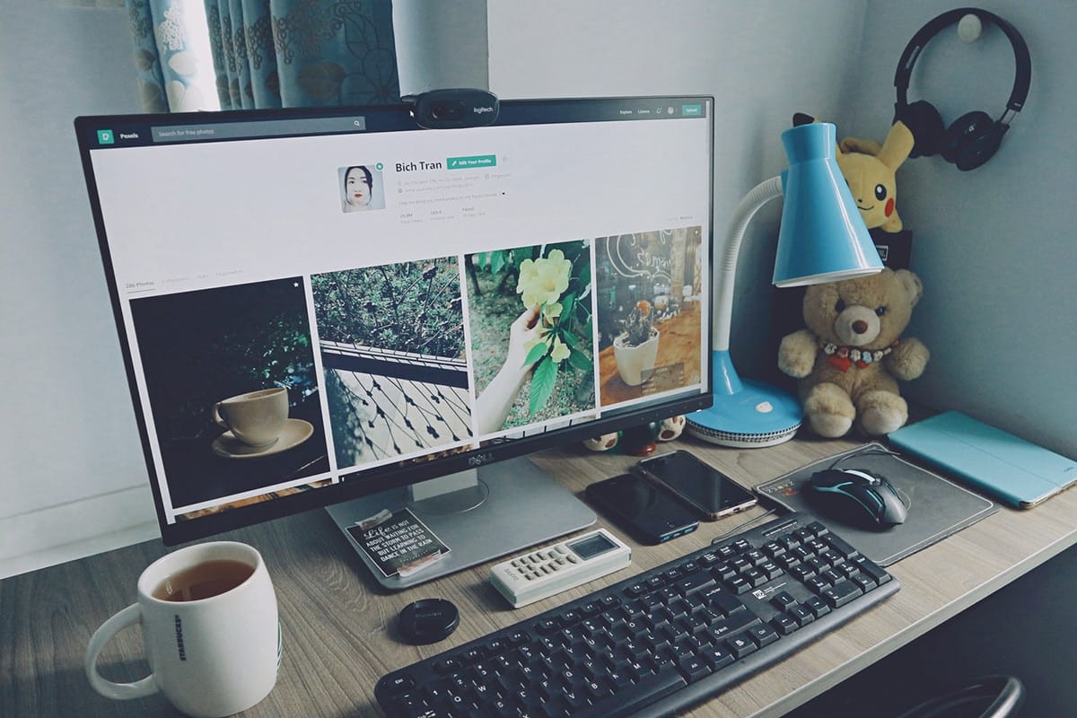A well-organized desk with a computer displaying a social media profile, surrounded by various office items including a cup of coffee, headphones, a notepad, a smartphone, a calculator, and some decorative objects.
