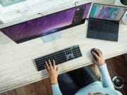 Person working at a desk with an ultra-wide monitor and a laptop connected to it, using a separate keyboard and mouse.