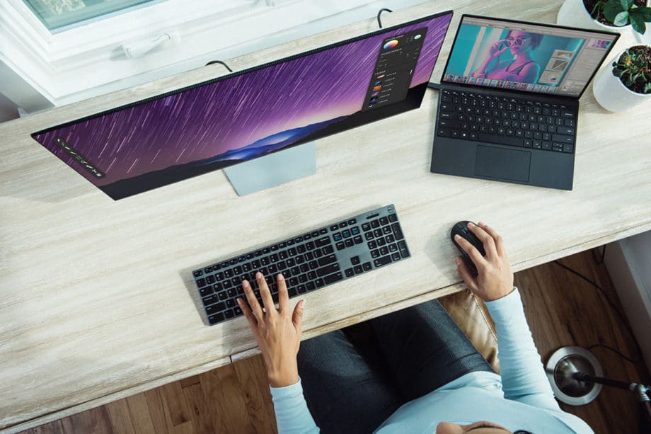 Person working at a desk with an ultra-wide monitor and a laptop connected to it, using a separate keyboard and mouse.
