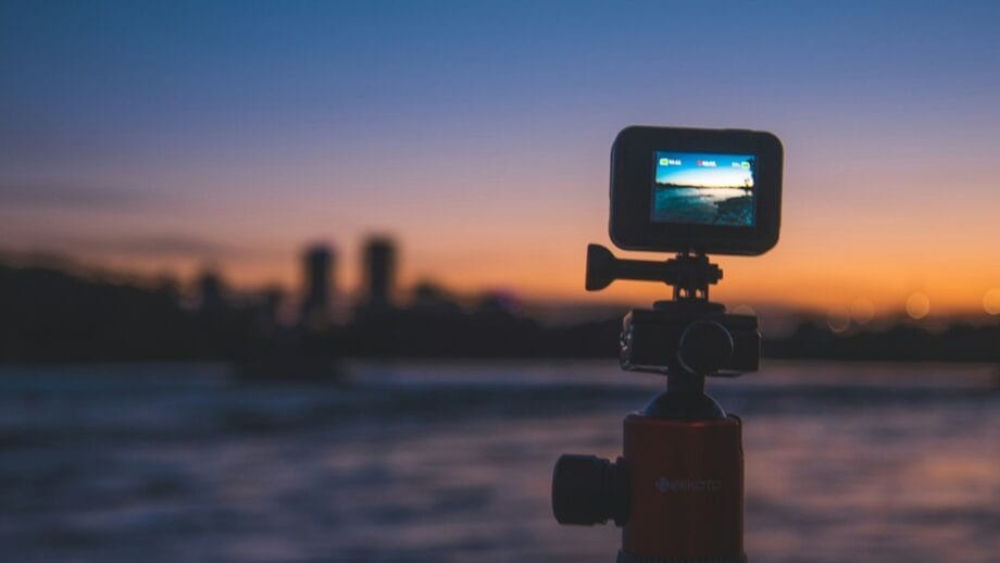 A small action camera on a tripod films a sunset over a city skyline by the water.