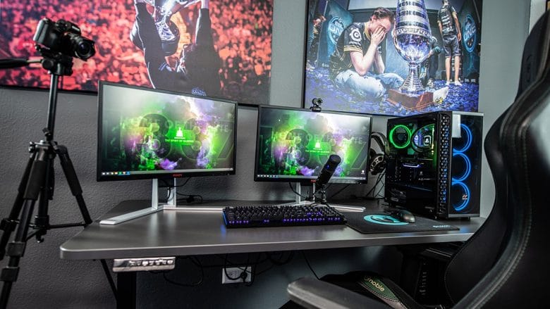 A multi-monitor gaming setup with led lighting, featuring peripherals and a camera on a tripod in a room with themed wall decor.