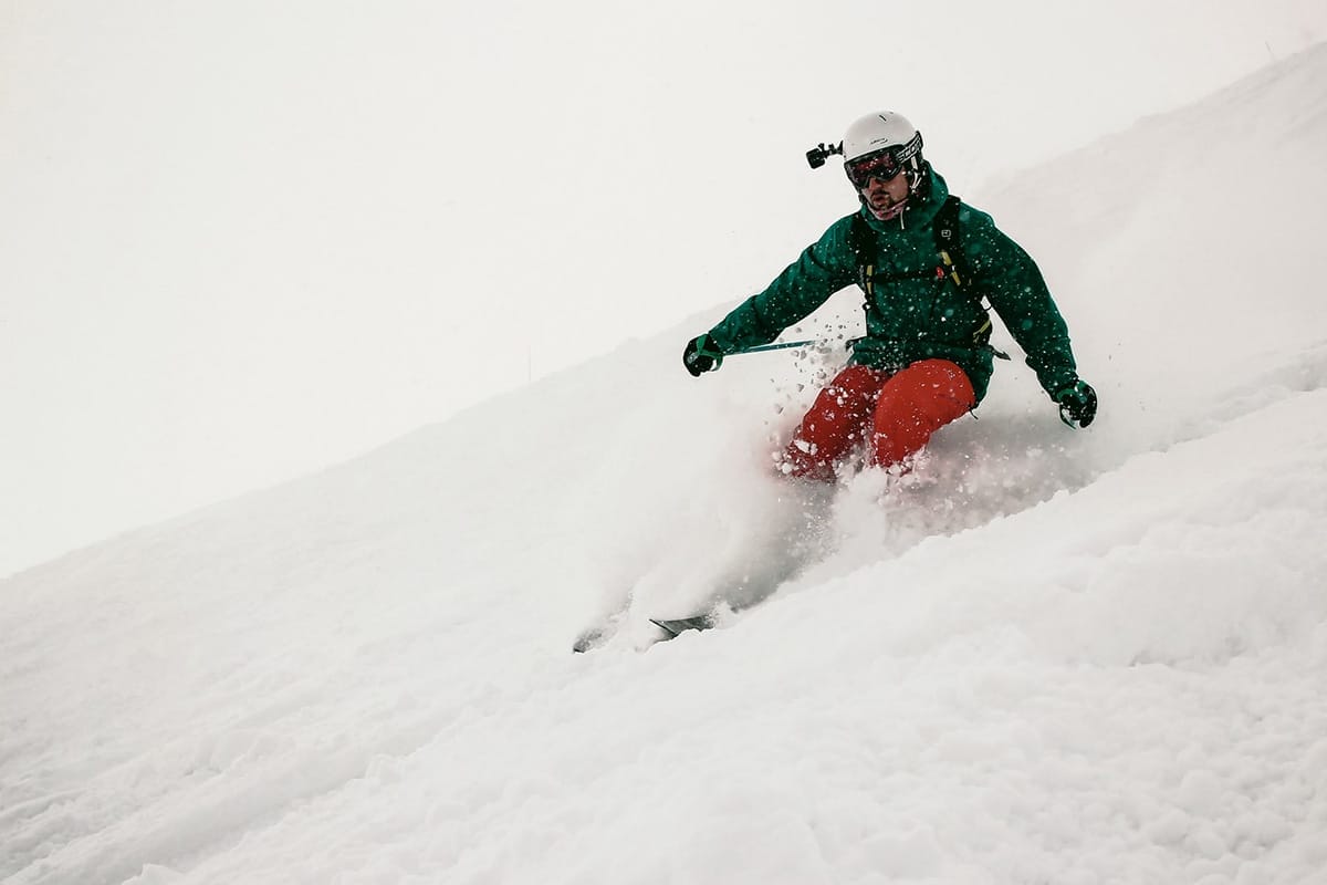 A person wearing a helmet and goggles skis downhill through deep snow, creating a spray of powder around them.