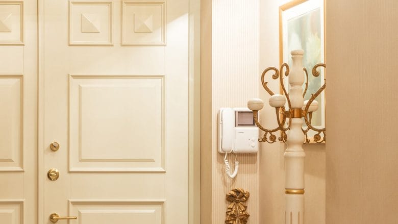 Elegant interior with a cream-colored door, intercom system, and decorative coat stand with gold accents.
