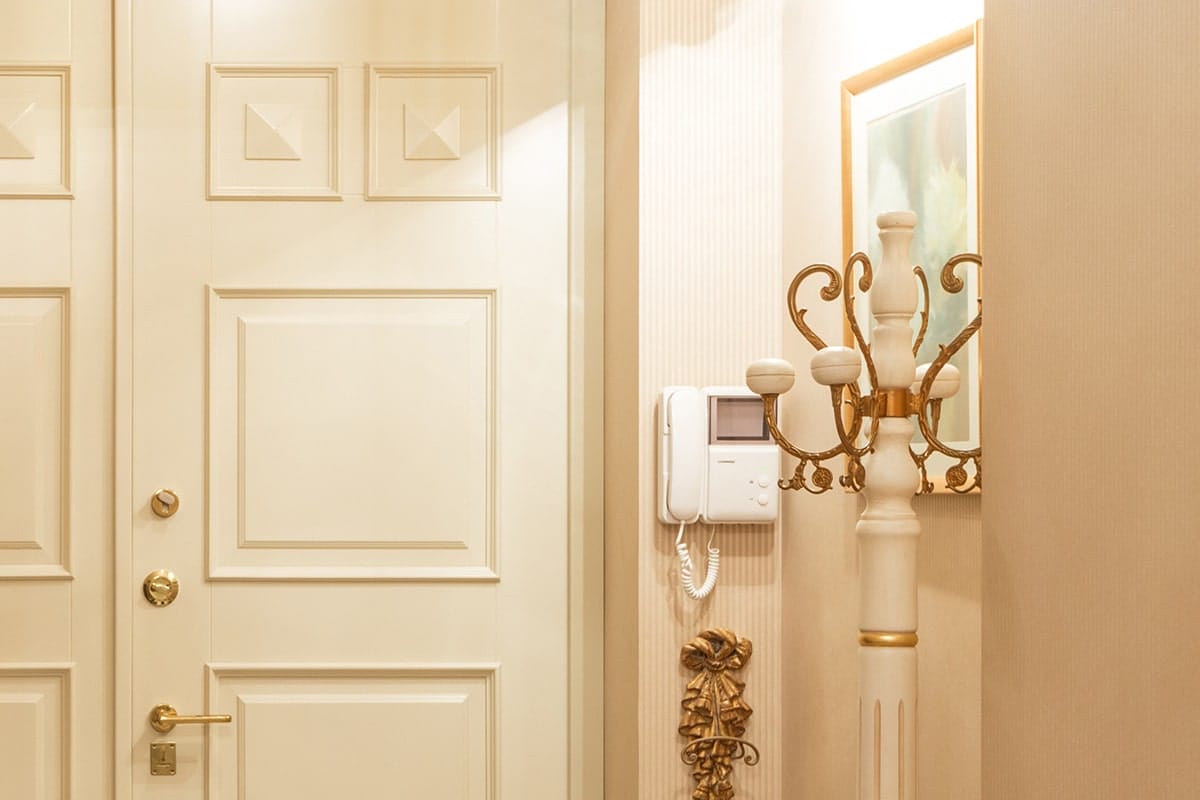 Elegant interior with a cream-colored door, intercom system, and decorative coat stand with gold accents.