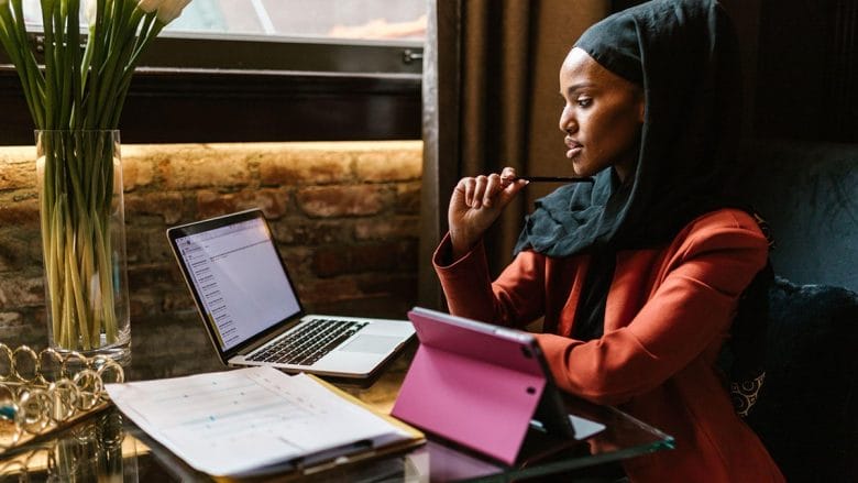 A woman wearing a hijab sitting at a table with a laptop.