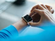 A person interacts with a smartwatch displaying the time, date, and notifications.