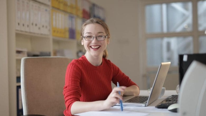 A smiling woman sitting at a desk with a laptop.