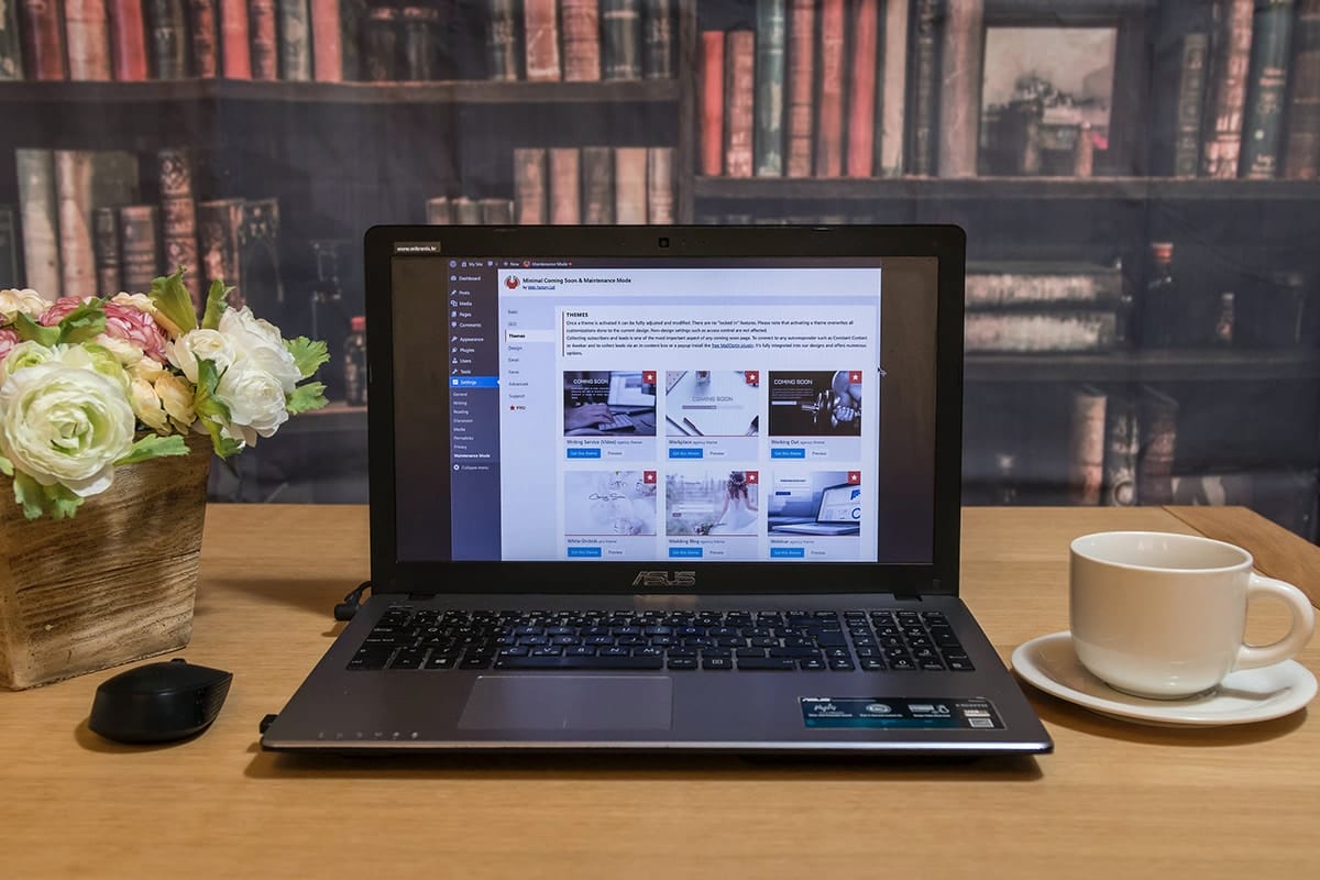 A laptop sits on a table next to a cup of coffee displaying WordPress dashboard.