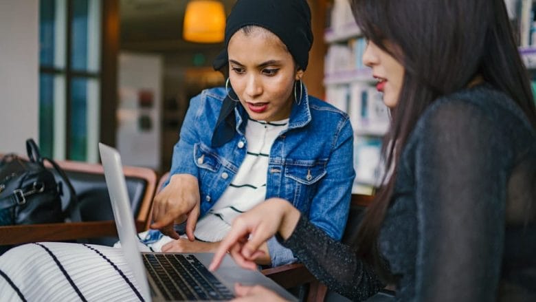 Two women looking at a laptop in a library.