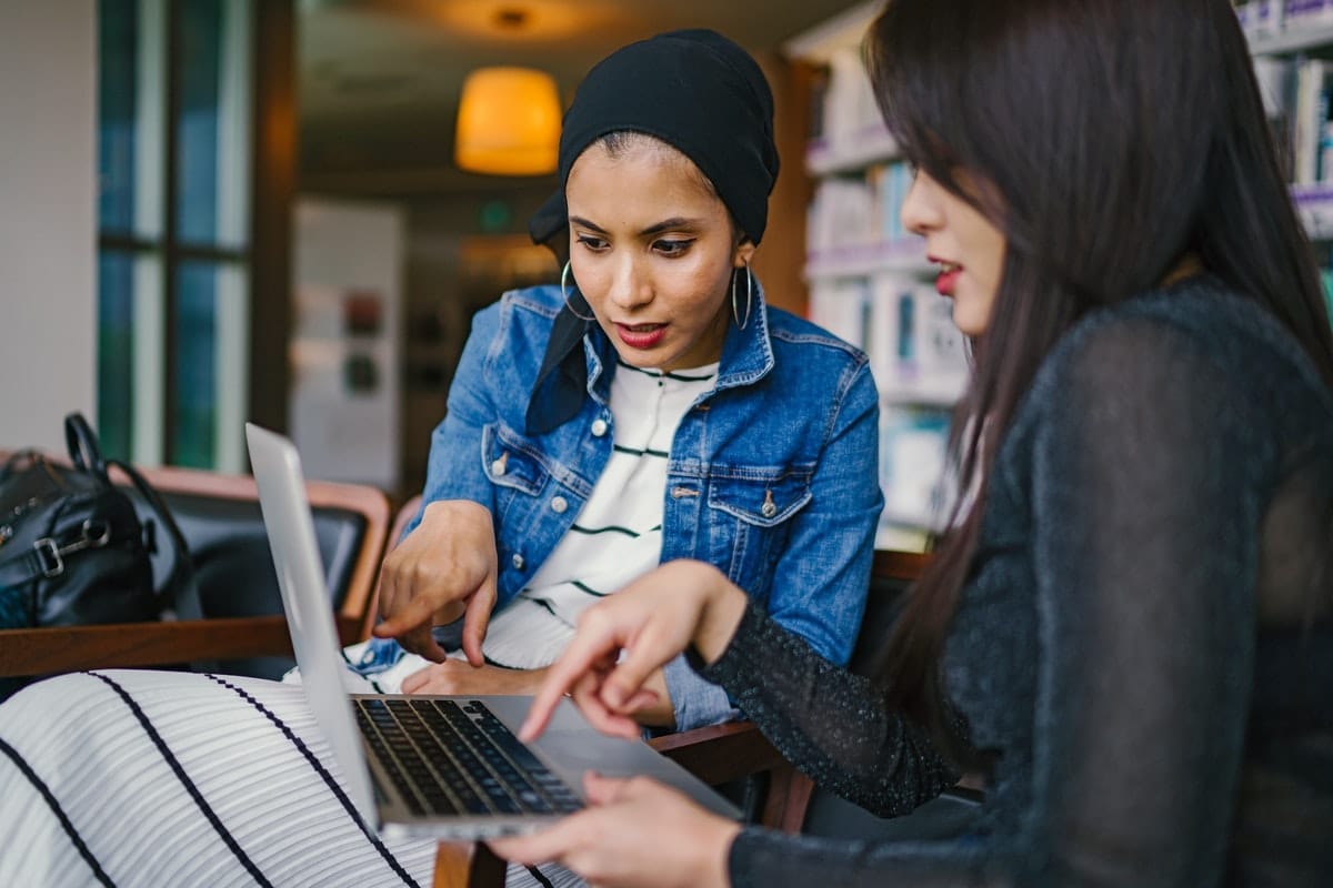 Two women looking at a laptop in a library.