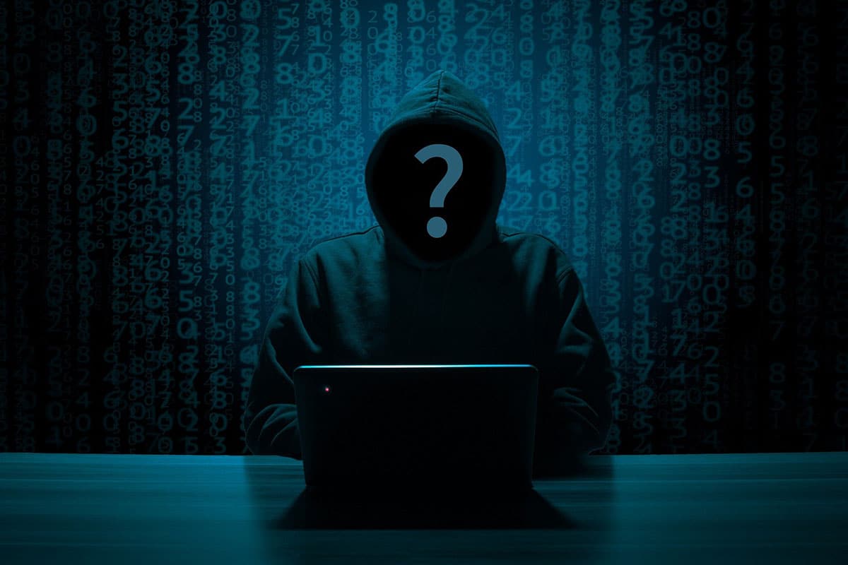 A hooded figure at a laptop with a question mark over their face, set against a backdrop of digital numbers.