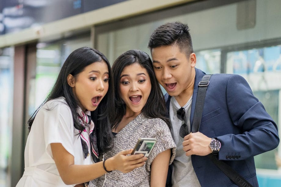 Three asian men and women looking at a cell phone.