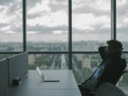 A man sitting at a desk with a laptop in front of a window.