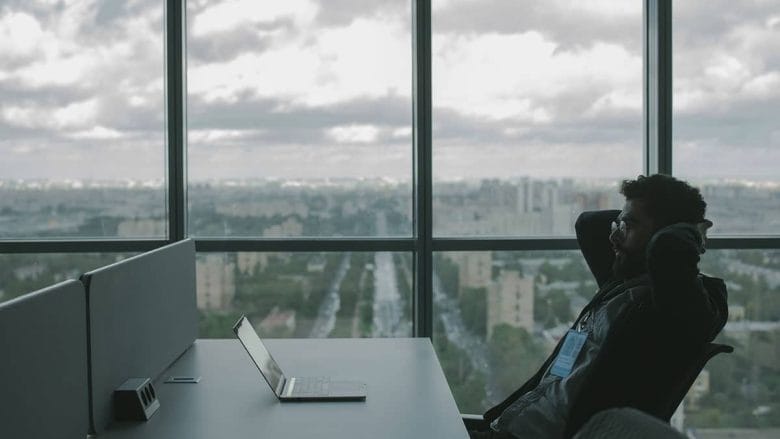 A man sitting at a desk with a laptop in front of a window.