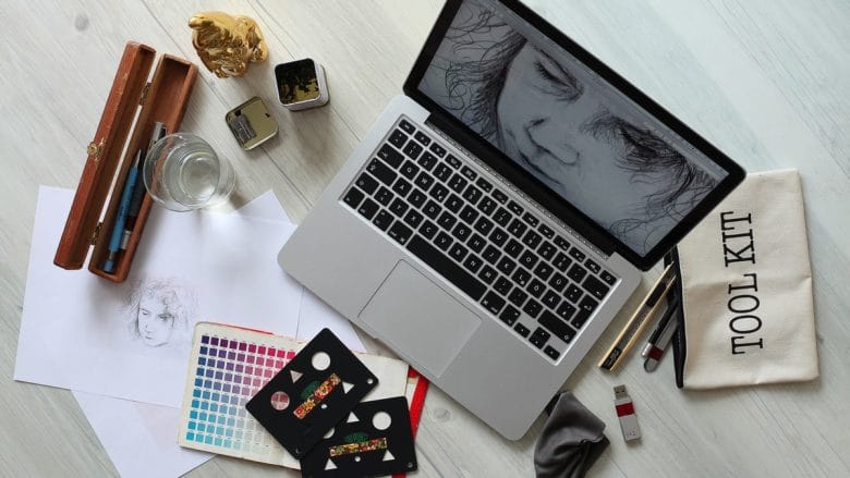 A laptop sits on a table next to art supplies.