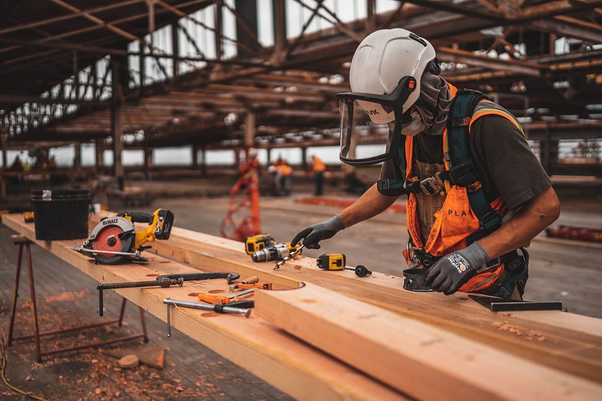 A construction worker is working on a wooden plank.