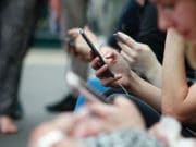 Close-up of multiple people using smartphones while sitting in a row, focusing on hands and phones.