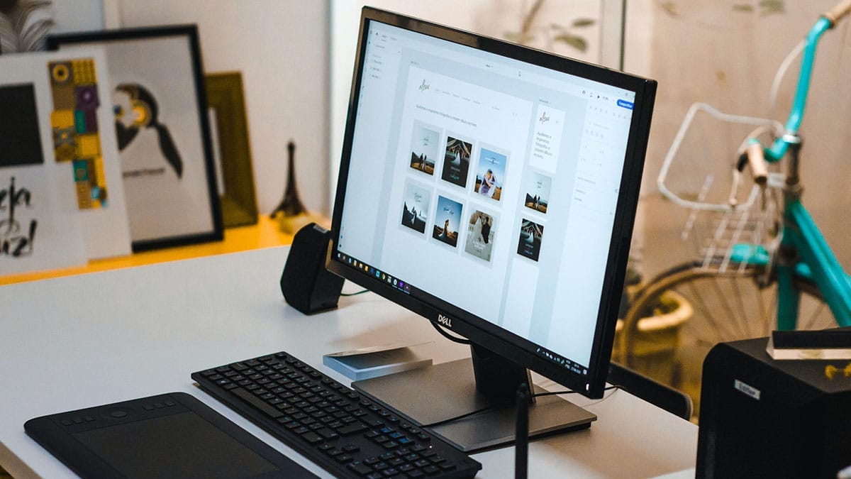 A tidy workspace with a computer monitor displaying a gallery of images, a keyboard, a graphics tablet, and some office supplies on a desk.