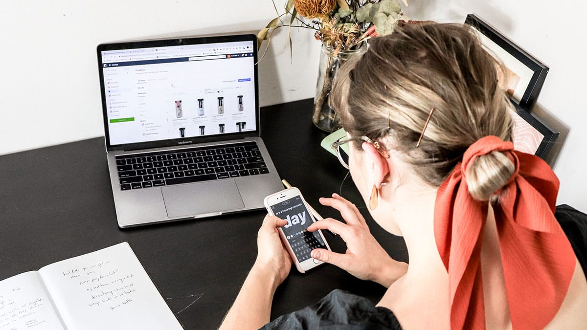 A woman sitting at a desk with a laptop and a cell phone.