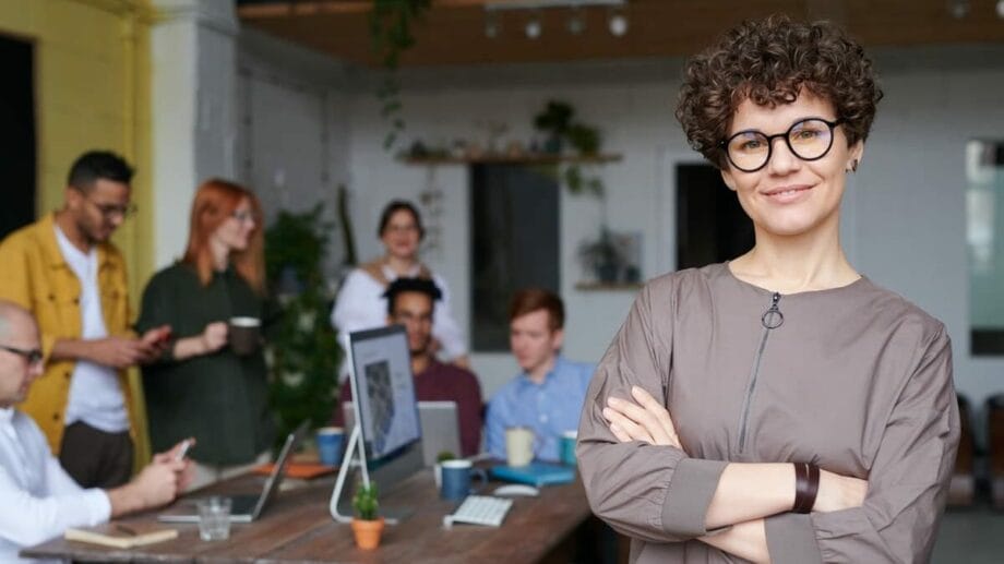 A woman in glasses standing in front of a group of people.