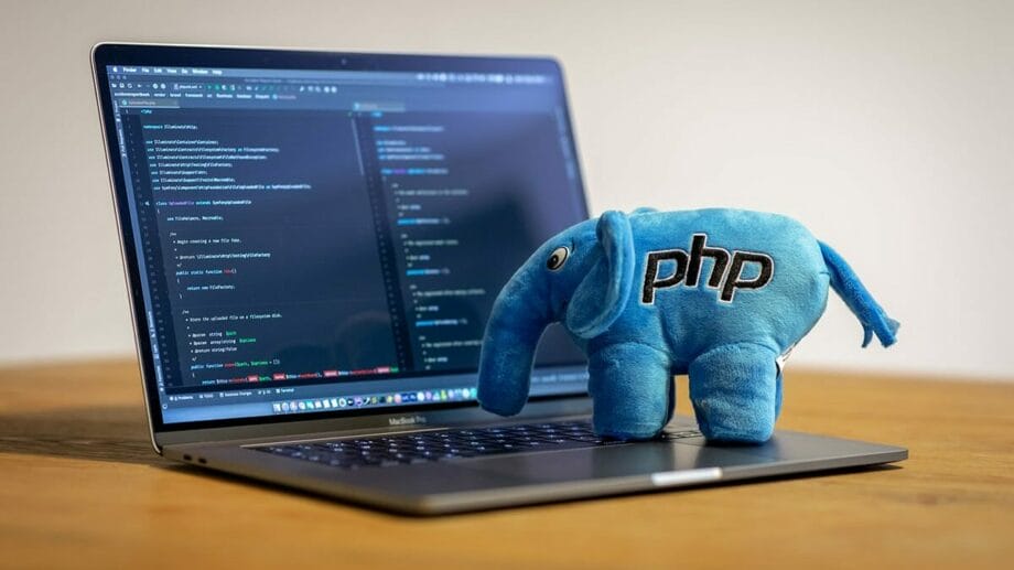 A stuffed elephant with the word PHP on it sits on top of a laptop.