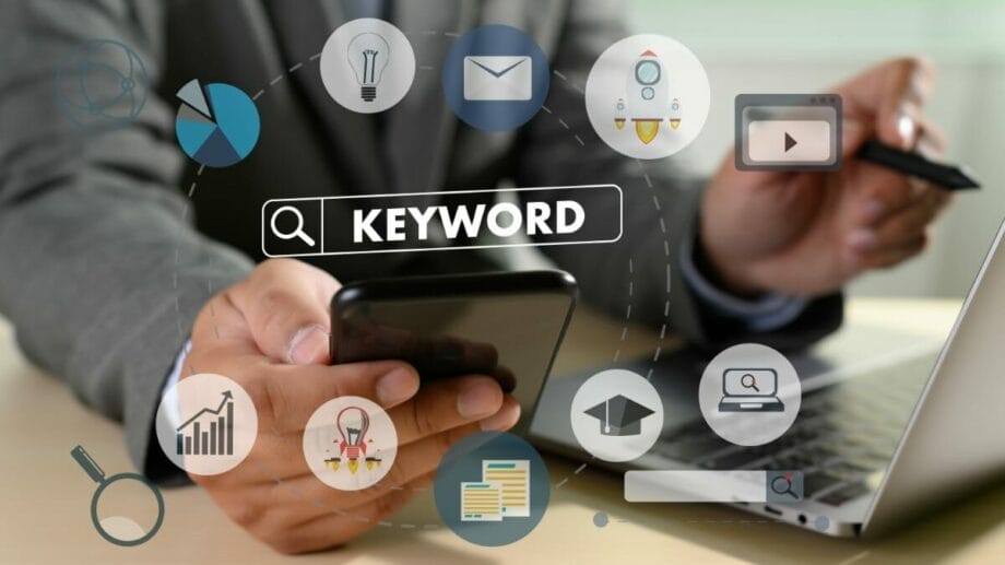 An image of a businessman using a laptop and mobile phone with the word keyword on it.