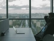 A man sitting at a desk with a laptop in front of a window.